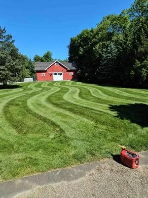 Striped lawn mowing pattern on large residential yard with red house and mature trees
