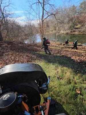 Cleared wooded riverside property with removed vegetation and debris, team working on sloped terrain